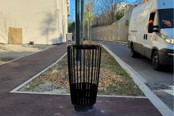 Corbeille de propreté urbaine noire installée sur un trottoir.