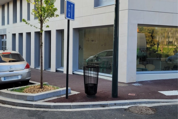 Corbeille de propreté noire à côté d’une piste cyclable en ville.